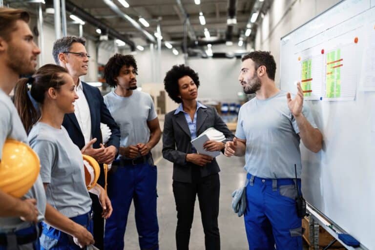 Young manual worker presenting new business strategy to company managers and his colleagues in a factory.